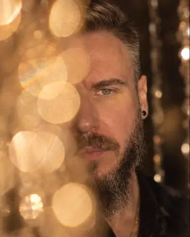 Half of a bearded man's face hidden behind huge golden discs of light, one eye in sharp focus