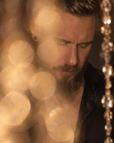 A bearded man looks down as his face dissolves into soft champagne-colored discs of light