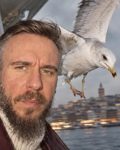 A seagull frozen by flash right beside a bearded man's face, the Istanbul shoreline smeared behind