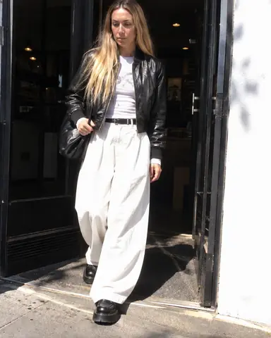 A woman with long blond hair steps out of a shop doorway into sun, half her face shaded, the street behind blown white