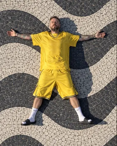 Top-down drone view of a bearded man lying on Copacabana's wave mosaic, arms spread, a long morning shadow