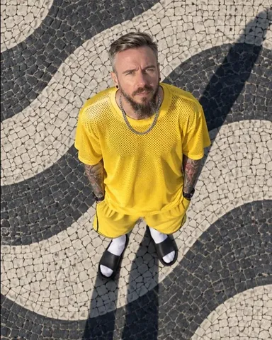 Lower drone shot of a bearded man standing and looking up, the Rio wave mosaic pattern all around him