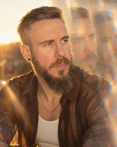 Tight portrait of a bearded man at golden hour, face three-quarters and sharp, two prism echoes drifting right