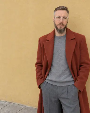 Waist-up view of a man pushed to the right edge, squared rust-red shoulders below, a plain ochre wall on the left