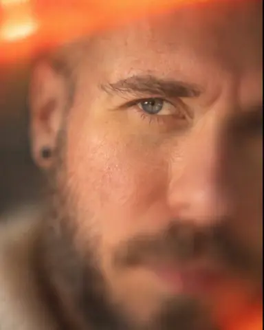 Close portrait of a man with only the left eye and brow sharp in a diagonal band, an orange light leak above