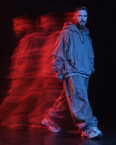 Full-length bearded man frozen sharp in blue light on the right, a smeared red ghost of his step streaming left