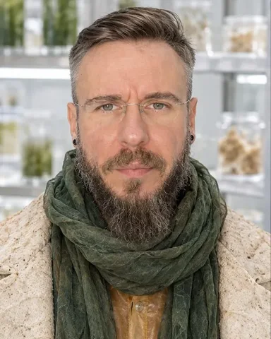Head and shoulders of a bearded man with a deep green algae-silk scarf wrapped high, calm frontal gaze