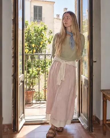 A woman with long blond hair leans in an open balcony doorway, backlight rimming her pistachio knit, face soft in fill flash