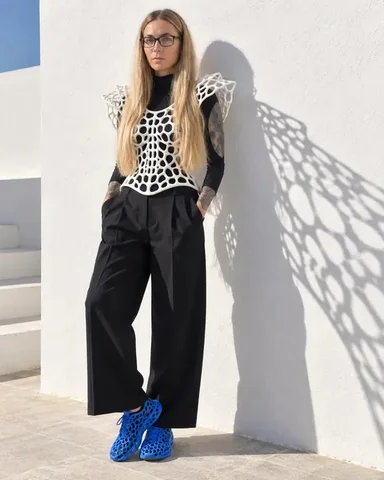 A woman with long blond hair in a white lattice vest and glasses, close up, lattice shadows falling across her face and wall.