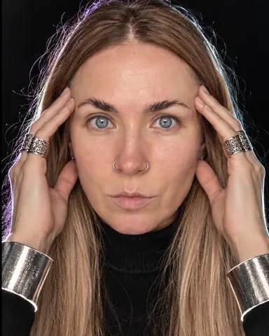 A woman with long blond hair, fingertips at her temples, rim light on her jaw and fingers reversed into silver lines