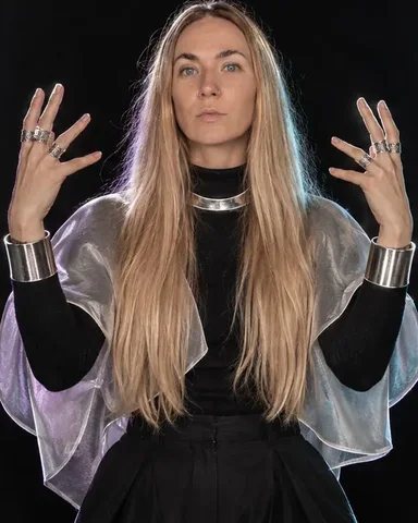 Fingers in stacked filigree silver rings on a rigid silver collar, each metal edge reversed into a thin white line
