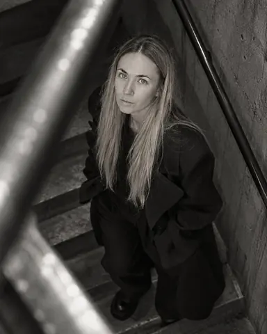 A blurred steel handrail cuts across the frame as a woman with long blond hair looks up from the stairs below