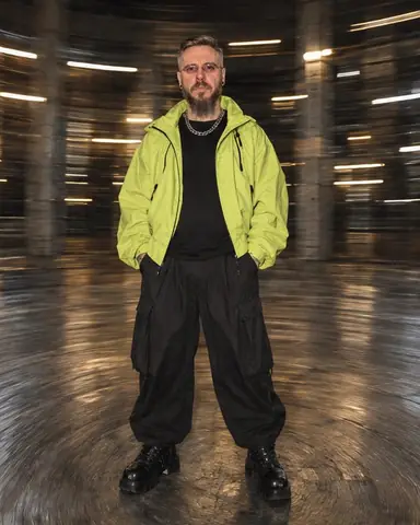 A man in an acid-lime jacket stands sharp at the center of a circular vortex of warehouse floor and light arcs