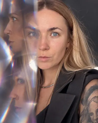 Half the frame refracted: a woman with long blond hair looks out sharp while her profile repeats twice through the glass