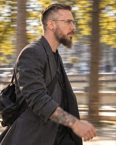 Half-length profile of a bearded man walking briskly past a row of trees whose trunks smear into stripes