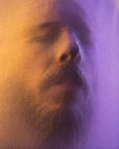 The soft shadow of a man's full figure on a glowing white scrim, doubled in amber and violet