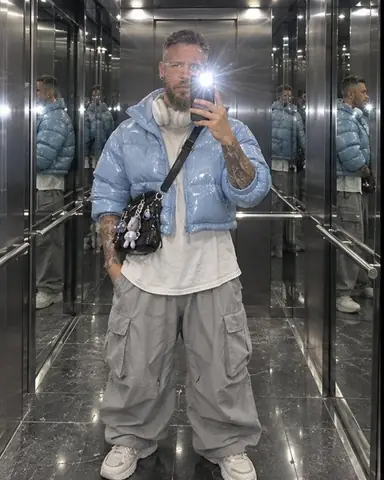 Full-length mirror selfie of a bearded man in a baby-blue puffer, phone flash starburst, reflections repeating sideways