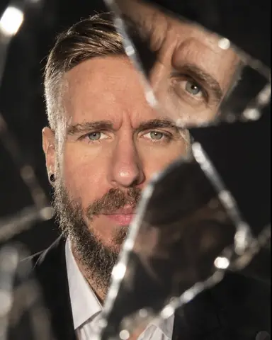 A bearded man's face split by three mirror shard edges, one eye repeated in a tilted fragment on dark ground