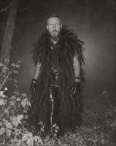 A bearded man looks straight at a trail camera from two meters, his eyes reflecting the infrared flash