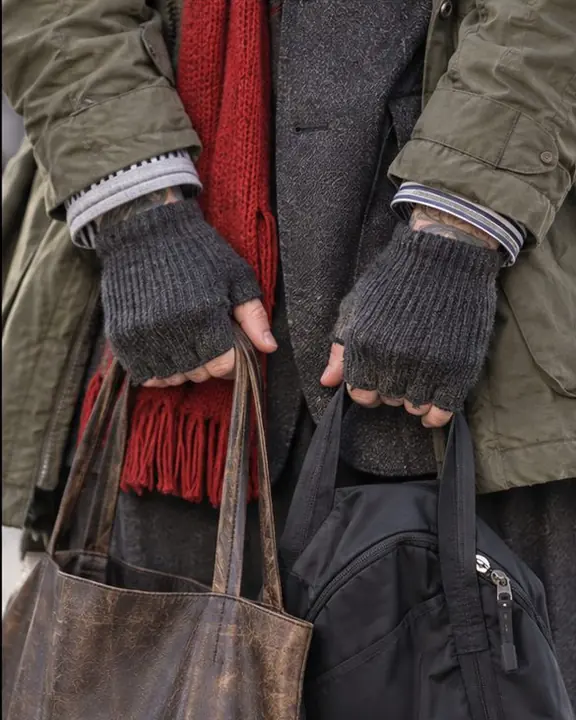 Telephoto close-up of hands holding two bags, parka, blazer and hoodie cuffs stacked, chains at the collar