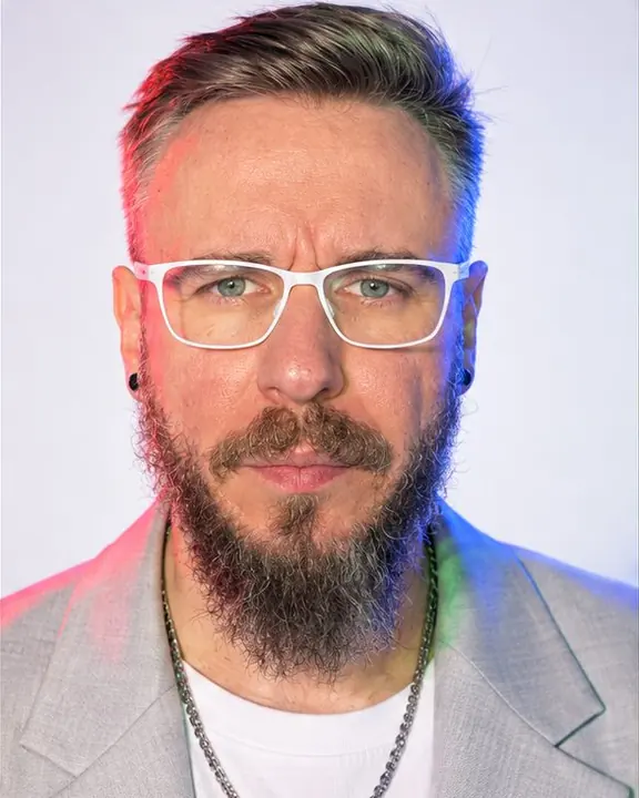Frontal head-and-shoulders of a bearded man, a red fringe of light on one cheek and a blue fringe on the other