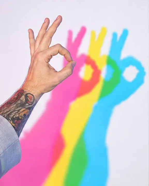 Close-up of a hand making a shape in front of a white wall, three colored shadow hands repeated behind it
