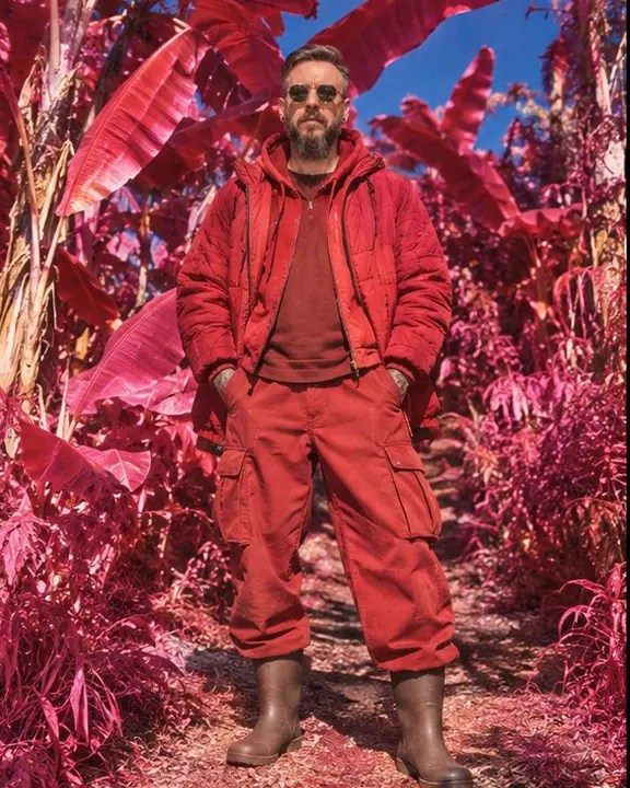 A bearded man in a red-rendered outfit stands on a path between giant magenta banana leaves under a cobalt sky
