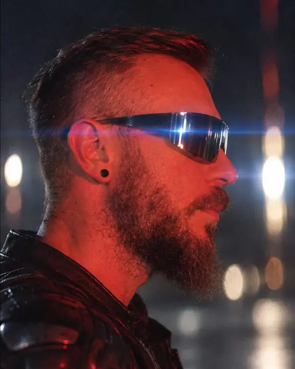 Profile of a bearded man in mirrored shield sunglasses, a blue anamorphic streak reflected in the lenses