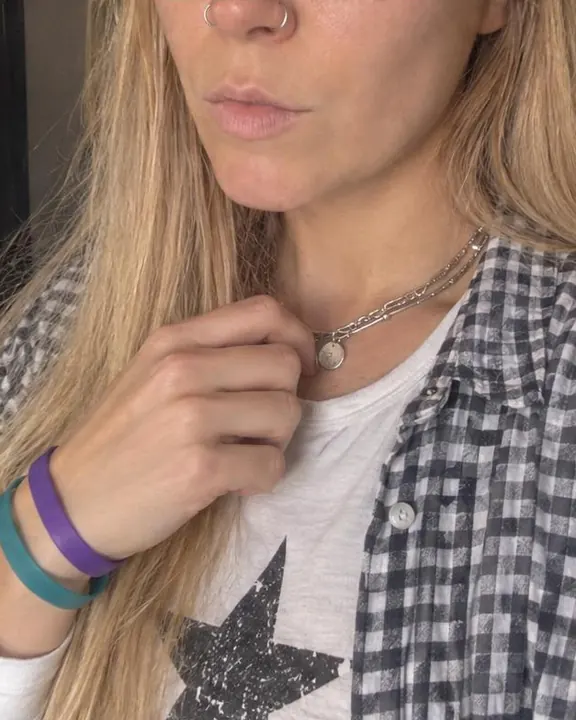 Noisy phone close-up of a hand at an open gingham collar, a silver curb chain with pendants and two rubber wristbands
