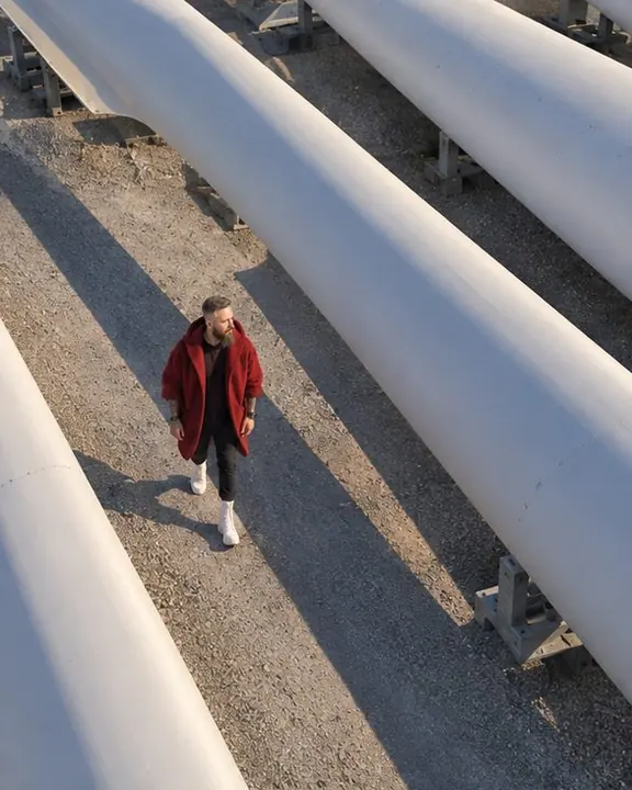 High diagonal aerial view of a man in red walking between two rows of huge white blades, a long shadow behind