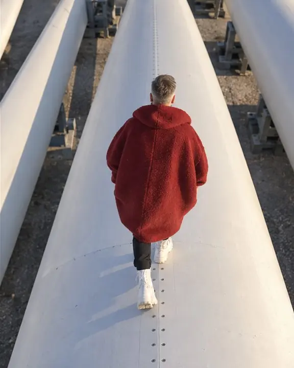 The rounded back of a deep red coat against a white turbine blade surface with bolts and seams