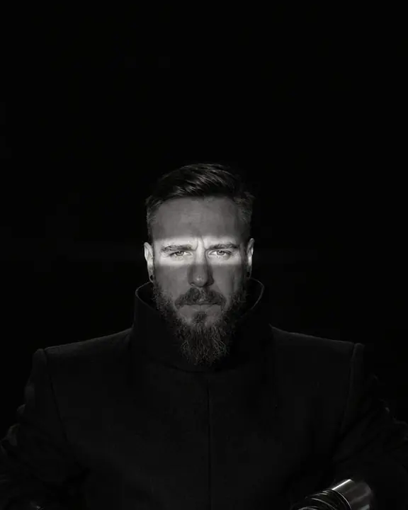 Half-length shot set low in the frame, light crossing squared black shoulders and eyes, the upper two thirds black