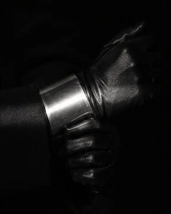 Close crop where a single band of light crosses only a wide silver cuff and a black leather glove