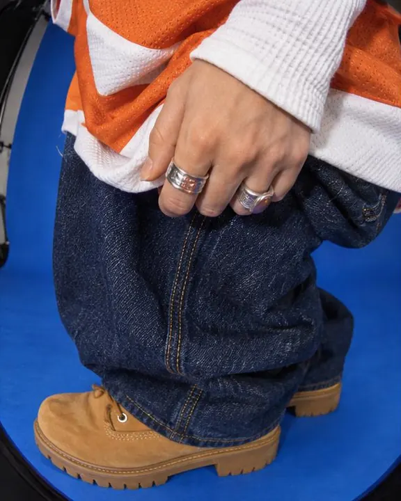 Strobe-lit close-up of a hand with stacked chunky silver rings gripping an orange jersey hem above indigo denim