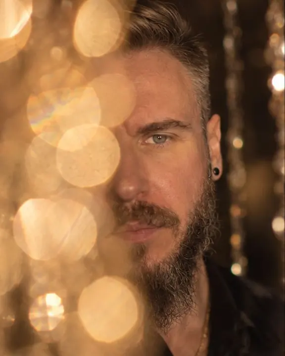 Half of a bearded man's face hidden behind huge golden discs of light, one eye in sharp focus
