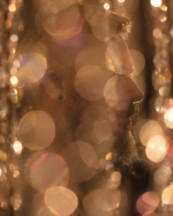 Overlapping discs of warm light fill the frame, a man's profile barely visible through them in the dark