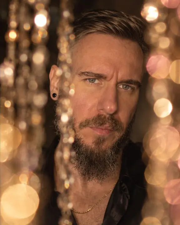 A bearded man's face sharp in a gap between two clusters of soft golden and rose bokeh discs