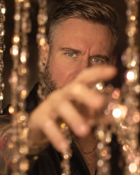 A man reaches a hand through a curtain of lights, large bokeh discs covering his lower face