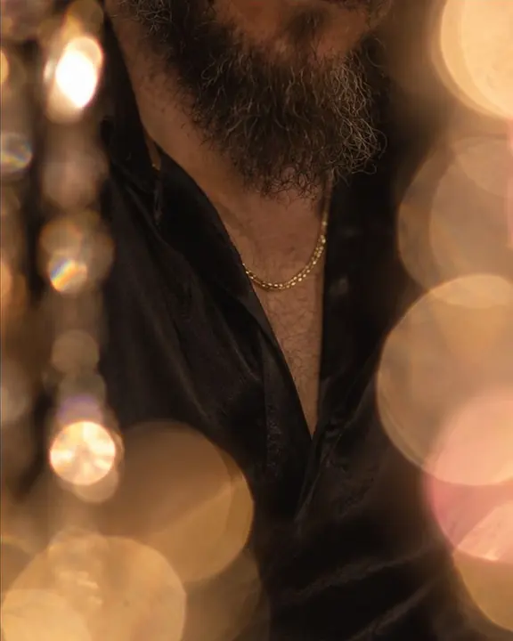 A thin gold chain on a black silk shirt glimpsed between enormous out-of-focus discs of light