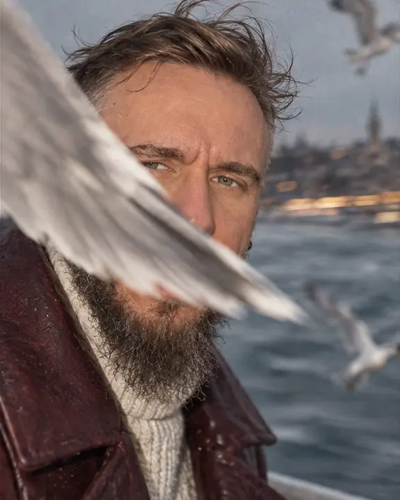 Close-up of a bearded man with wind in his hair as a gull's wing crosses the frame in flash