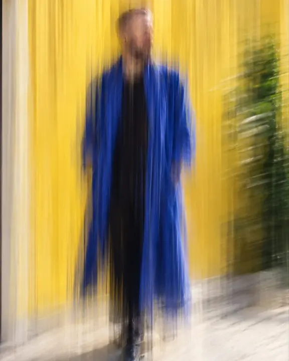 A man's full figure as a tall ultramarine streak against a yellow wall, his face only a soft hint