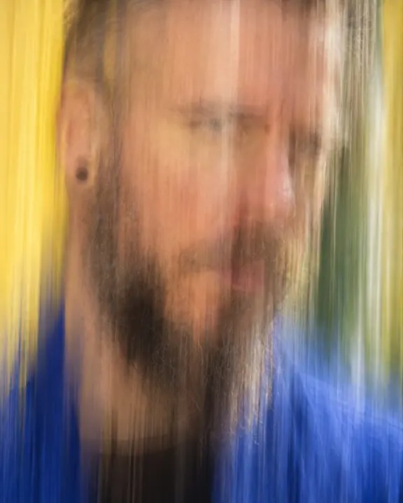 A close face of a bearded man streaked vertically by camera movement, barely readable