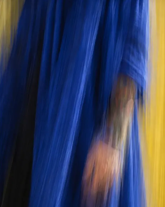 Ultramarine coat fabric stretched into vertical painterly streaks by a moving camera