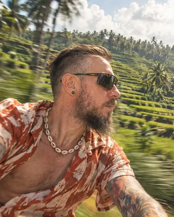 A man in a rust and cream linen shirt rides past rice terraces streaking green, his shirt flapping in the wind
