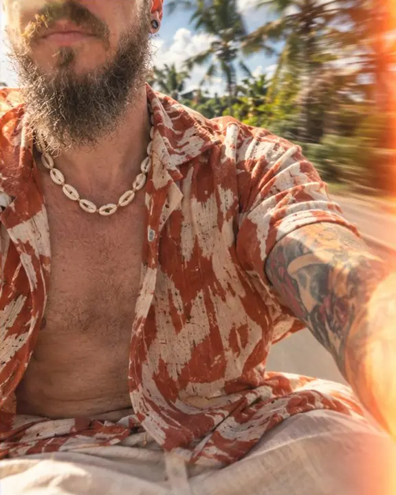 A shell necklace on an open rust and cream printed linen shirt with orange light leaks across the frame