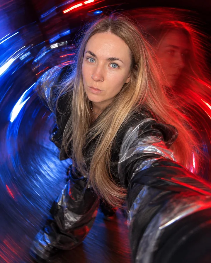 A woman with long blond hair reaches toward the lens, her face sharp in a red and blue spiral, a red echo beside it