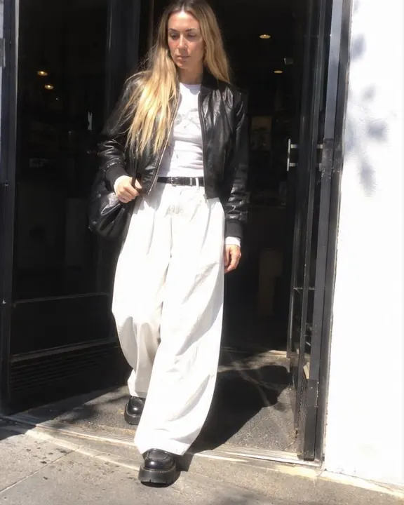 A woman with long blond hair steps out of a shop doorway into sun, half her face shaded, the street behind blown white