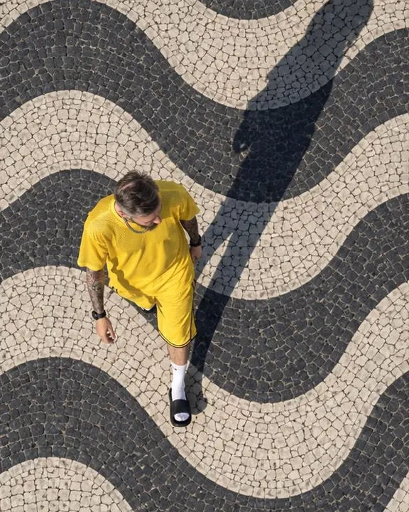 Aerial view of a man in a canary-yellow jersey walking along a black-and-white wave line, shadow stretching