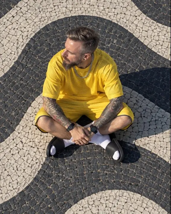 A man in a yellow mesh jersey sits cross-legged in the center of a curve of the wave mosaic, seen from above