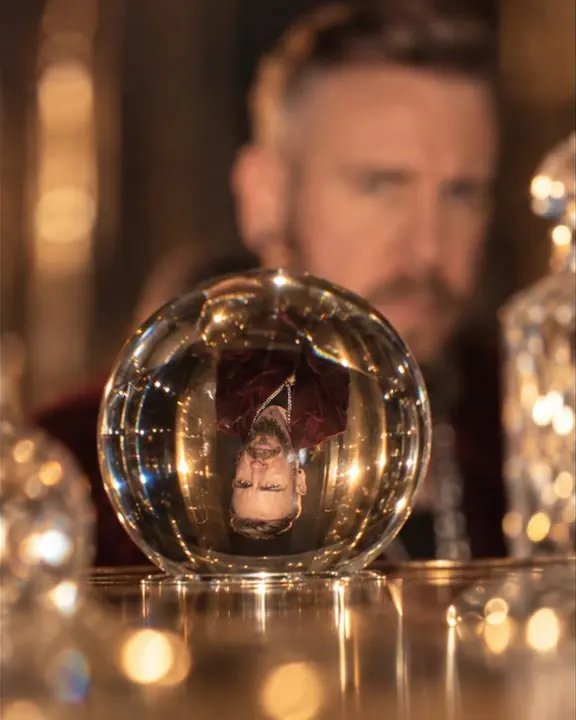 A tiny inverted image of a man glows inside a crystal paperweight, the real man blurred in burgundy behind